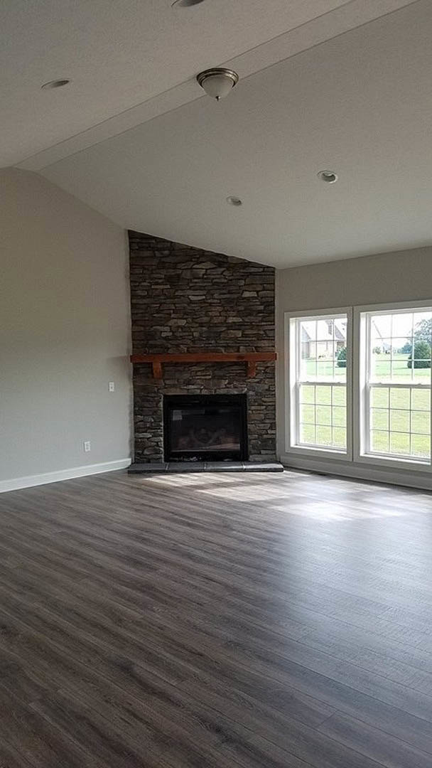 Hardwood floor and plaster walls in a living room featuring a fireplace with a wood beam mantel, large window, and ceiling detail.
