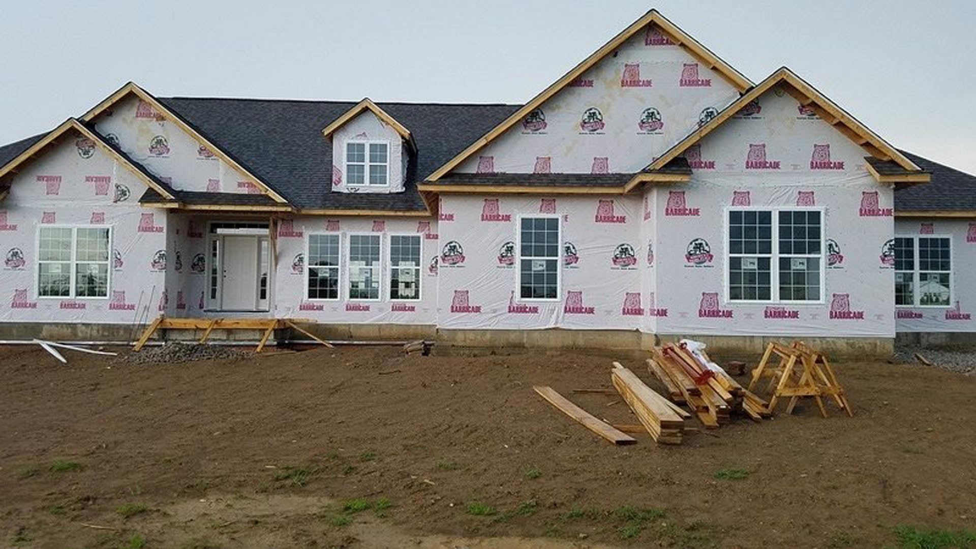 Modern cottage-style home with gray siding, covered roof, square-paned window, white door with glass panels, and stacked wood planks on the ground outside