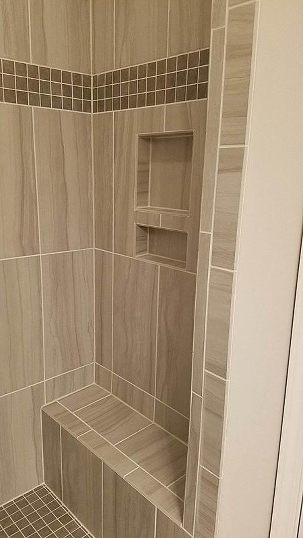 Tile shower with built-in wall shelf and bench, featuring light ceramic tiles and modern plumbing fixtures.
