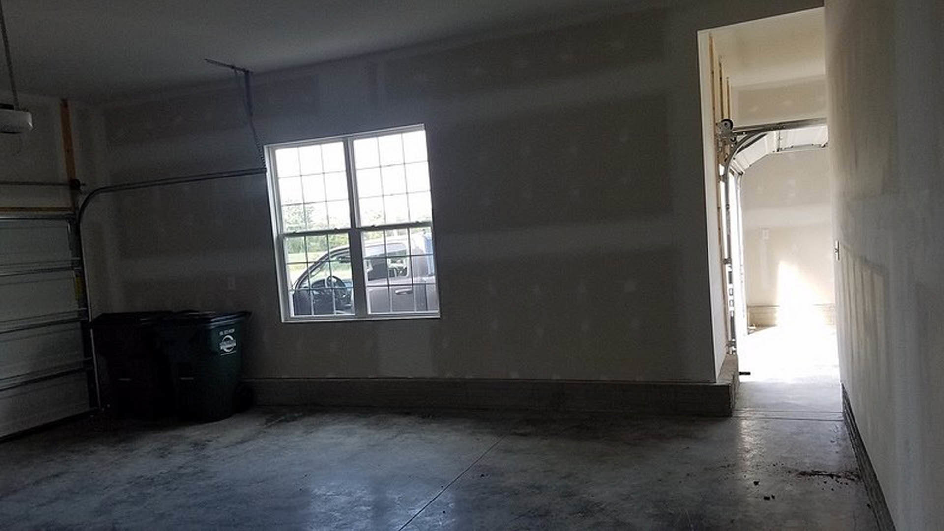 Bright room with plaster walls, large window, wood flooring, white door, and metal garbage can near the corner