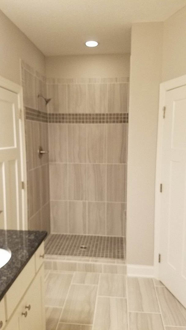 Bathroom with white tile shower, glass enclosure, modern vanity with undermount sink, chrome faucet, and light gray floor tiles.