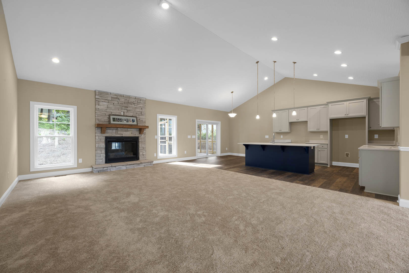 Spacious living room with plush carpet, central fireplace, open kitchen featuring blue walls, white countertops, black microwave, cabinetry, large window with outdoor view, and