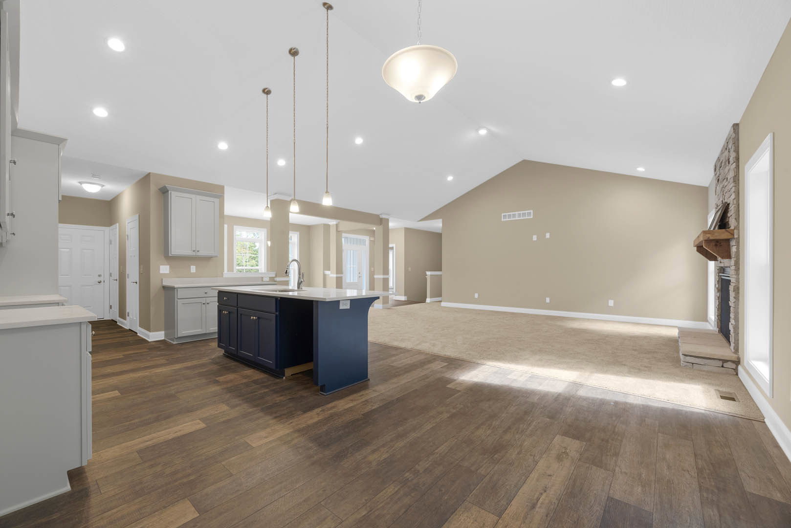 Spacious open floor plan featuring a central kitchen island with built-in sink, hardwood flooring throughout, white cabinetry with white trim, and modern light fixture above the