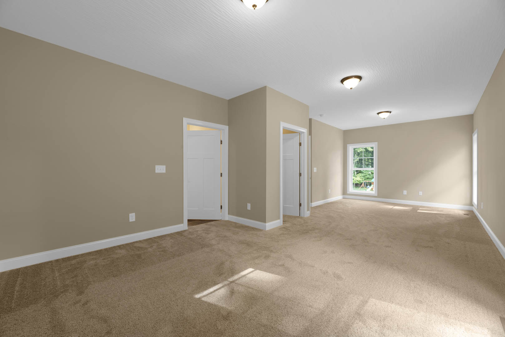 Beige walls, carpeted floor, white door with gold handle and frame, ceiling light fixture, window overlooking trees
