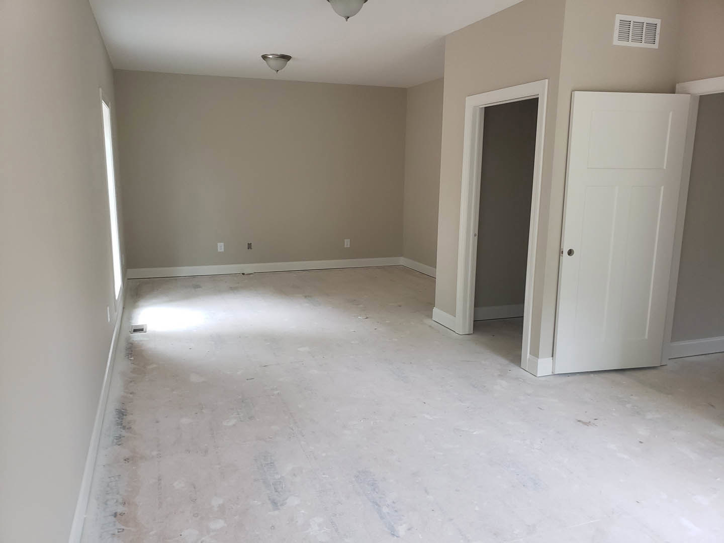 White-painted room featuring a white door with a silver doorknob, smooth plaster walls, white flooring, ceiling light fixture, and wall vent.