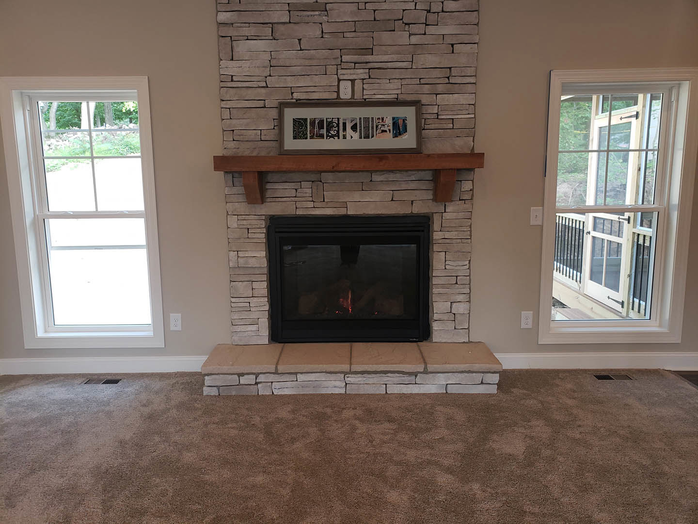Brick fireplace with black metal frame, burning fire, white-framed window, wood floor, built-in shelf, and neutral walls in cozy den.