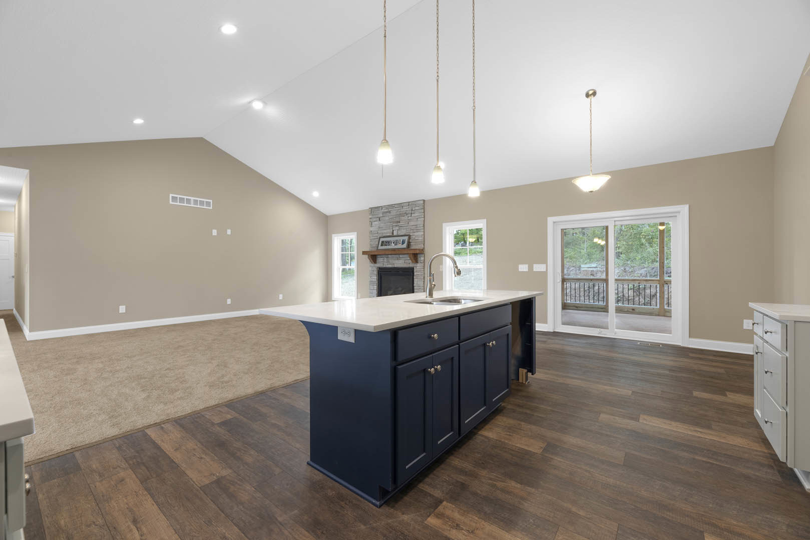 White quartz kitchen island with built-in stainless steel sink and modern faucet, light wood cabinetry, sliding glass door opening to forest view, wide plank flooring