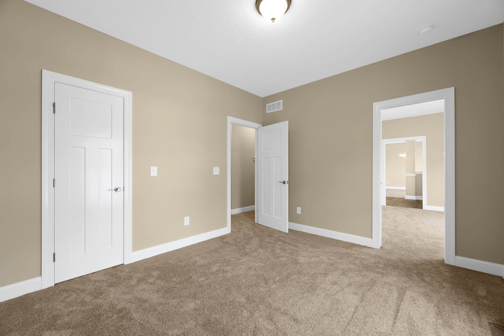Beige-walled room with white paneled door featuring silver handle, plush carpet flooring, white ceiling with recessed light fixture, and decorative crown molding