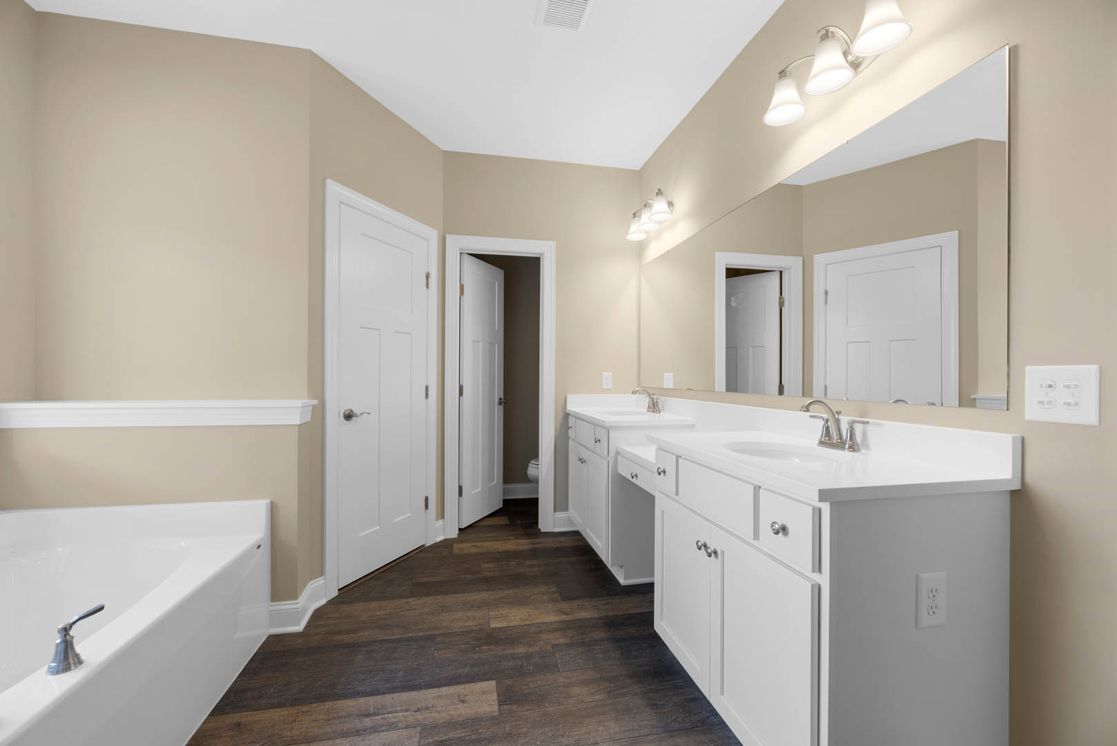 White bathroom with shaker cabinets, freestanding bathtub, silver faucet, white door and frame, light fixture, and tiled floor.