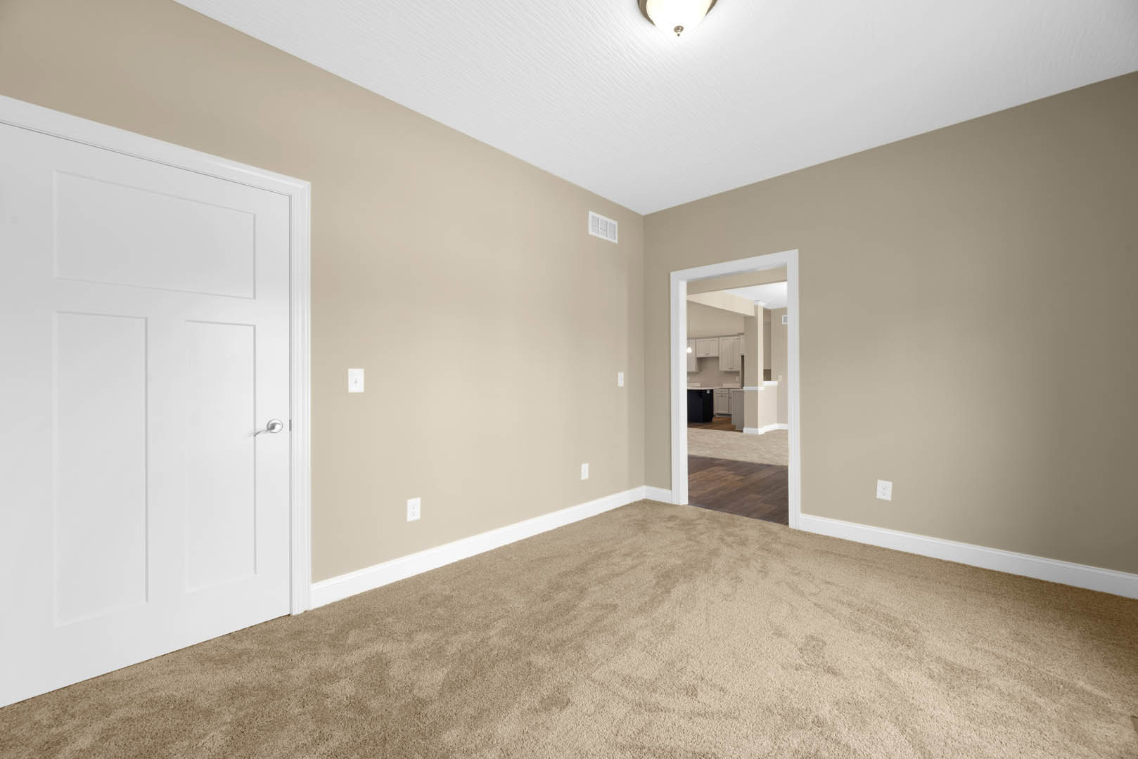 Beige carpeted room with white paneled doors, silver door handle, tan walls, white ceiling molding, and a white air vent