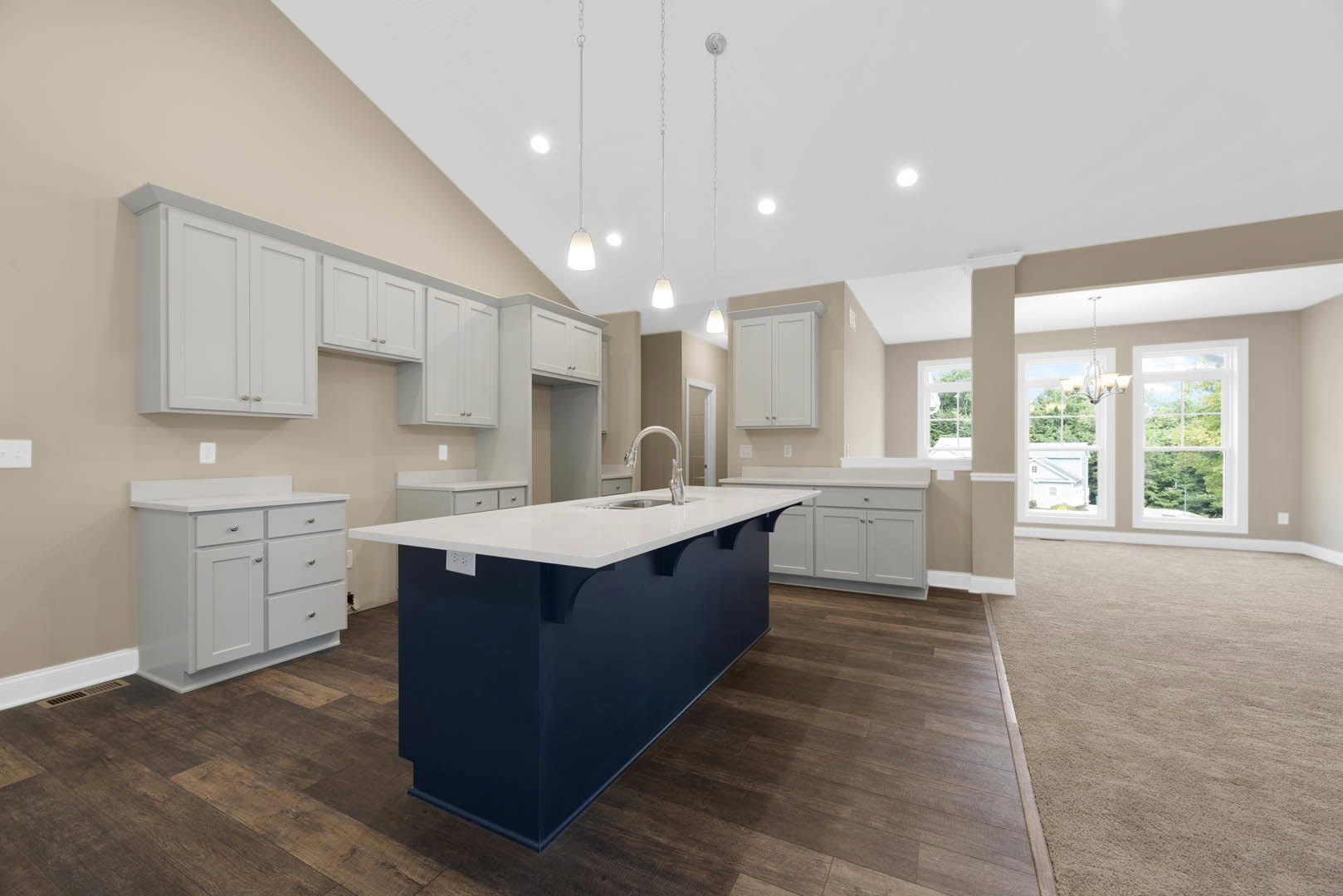 Blue kitchen island with built-in sink, white shaker cabinets and drawers, light tile flooring, white-framed window, and neutral wall finishes.