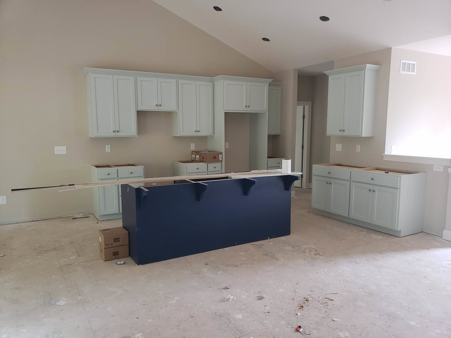 White kitchen cabinets with silver hardware, blue island with white countertop, wood ceiling beams, stainless steel sink, light hardwood floor, stacked brown moving boxes near