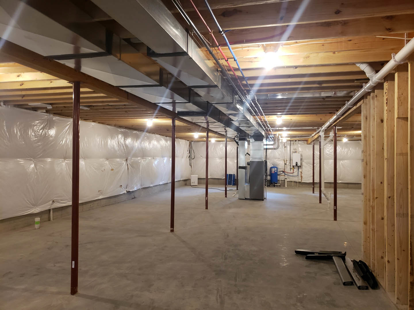 Spacious room featuring a large white wall, exposed metal beams and poles, concrete floor, and visible ceiling insulation.