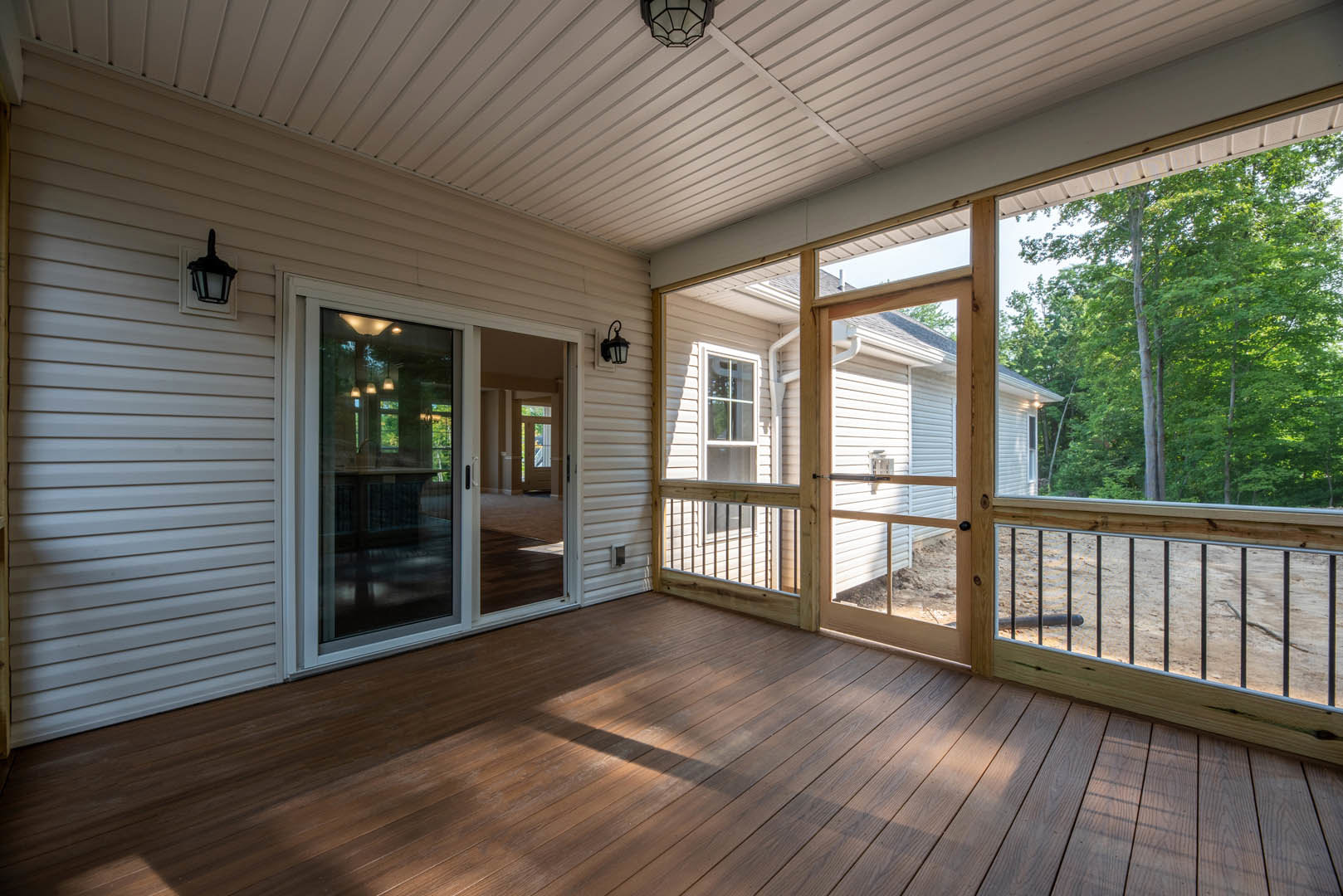 Wooden deck with horizontal railing, screen door leading inside, glass windows reflecting kitchen interior, close-up of outdoor lamp, wood plank flooring.