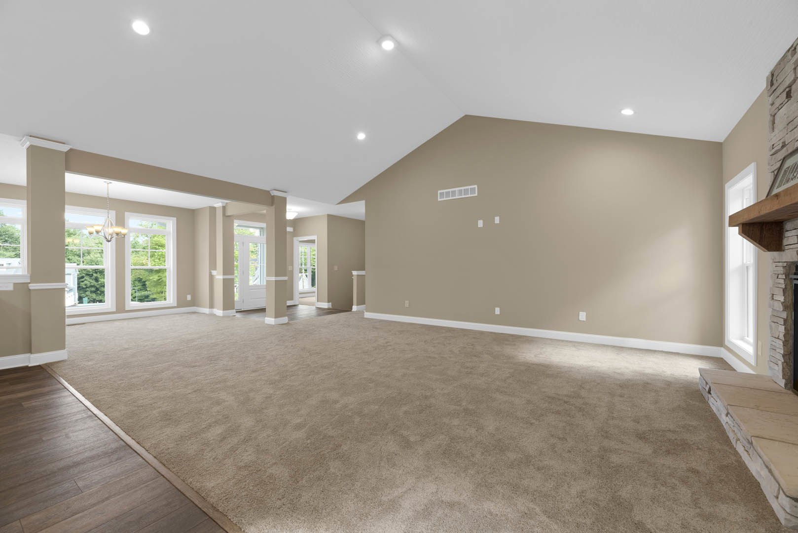 Spacious carpeted room with white walls, white ceiling with recessed lights, large window with white frame, and partial stone accent wall