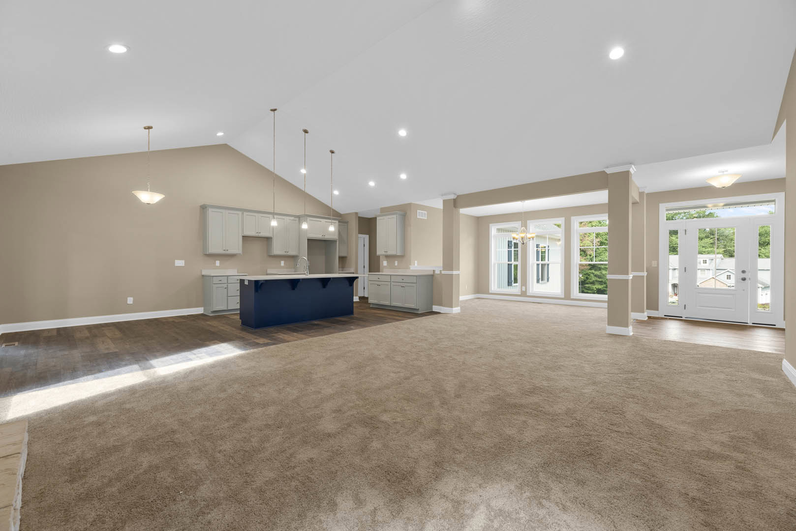 Spacious open floor plan featuring a carpeted living area, blue kitchen island and cabinets, white double doors with glass panes, blue accent wall with white shelves, and a high