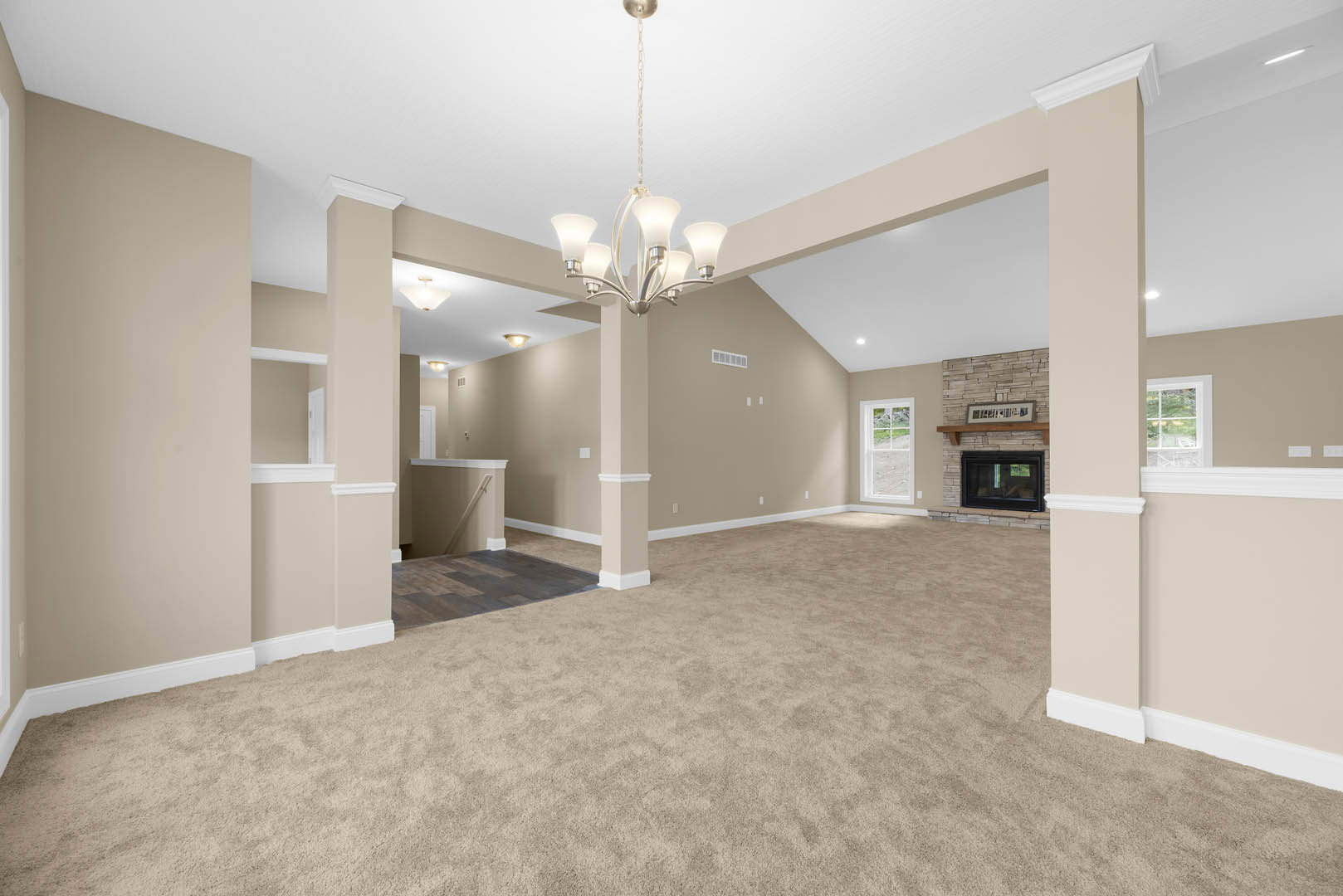 Living room with beige carpet, white-framed window, black fireplace with glass front, staircase with carpeted steps, and ornate chandelier hanging from plaster ceiling