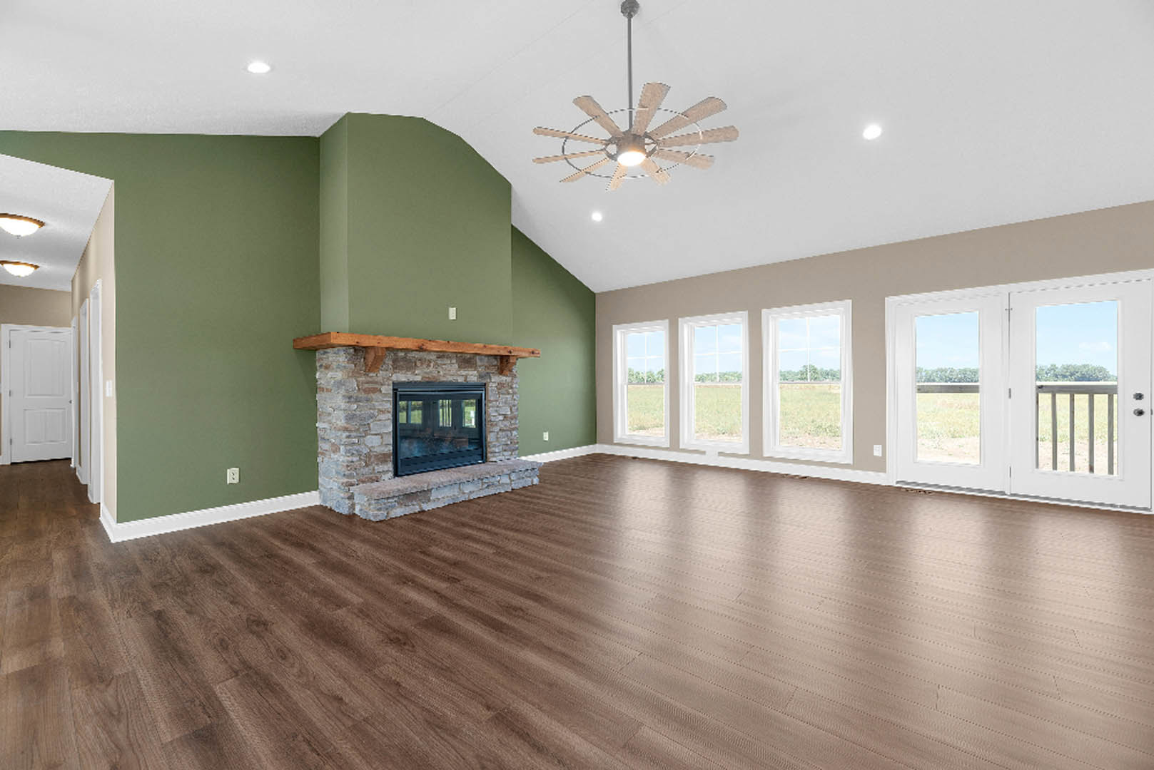 Living room with hardwood floors, white walls, wood mantel fireplace, ceiling fan with light, large window, and white door with silver knob
