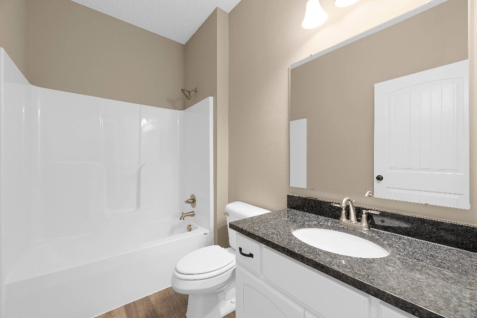 Modern bathroom with freestanding white bathtub, wall-mounted sink on grey tile countertop, white toilet, black door handle, and light-colored tile walls