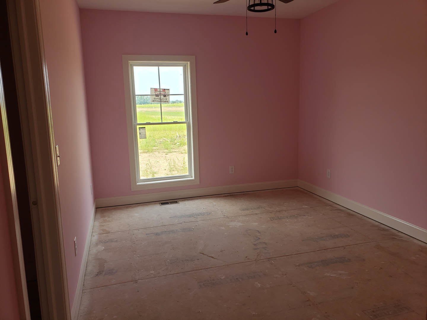 Pink plaster walls, white ceiling, window overlooking grassy field, light fixture, sign visible through glass