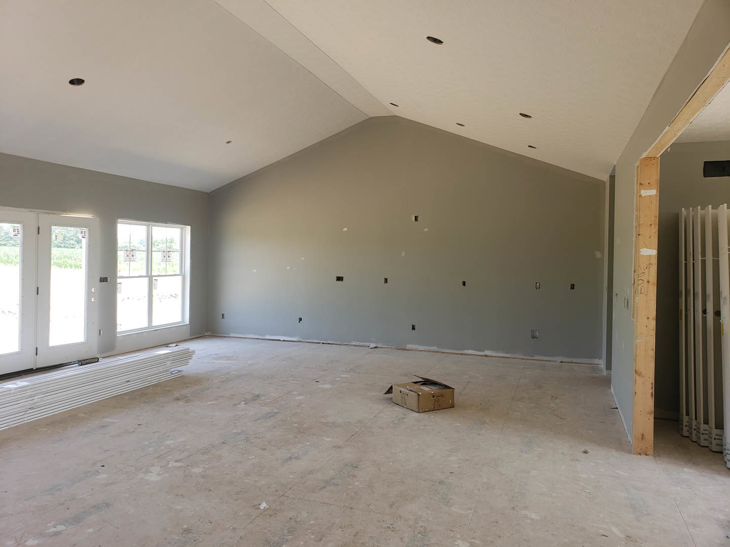Unfinished room with plaster walls, white plastic planks stacked near an open brown box, row of white metal bars, window displaying several signs