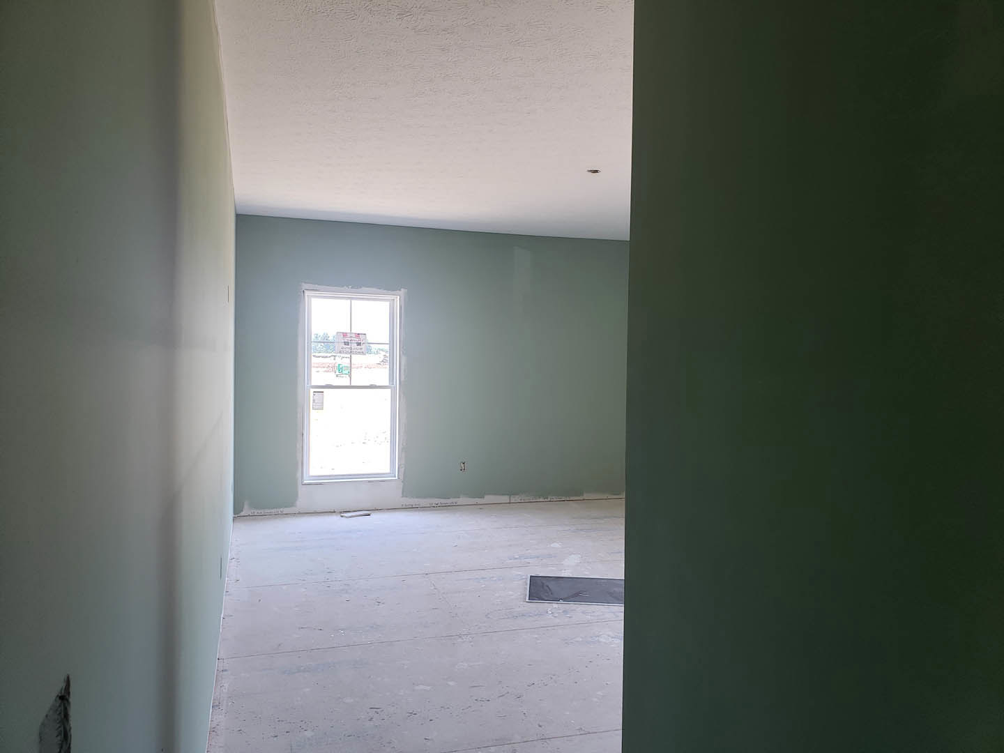Dark green accent wall and white plaster wall with mounted light fixture, large window with sign, tiled floor, and black surface detail in a residential interior.