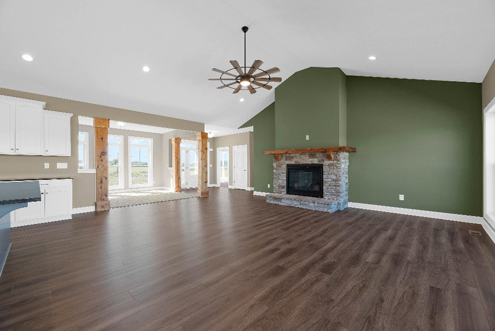 Spacious living room featuring hardwood floors, stone fireplace with wood beam mantel, ceiling fan with light, and neutral walls