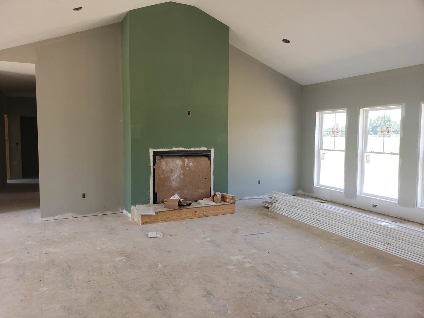Living room with green accent wall, white plaster fireplace, light wood flooring, and two windows.