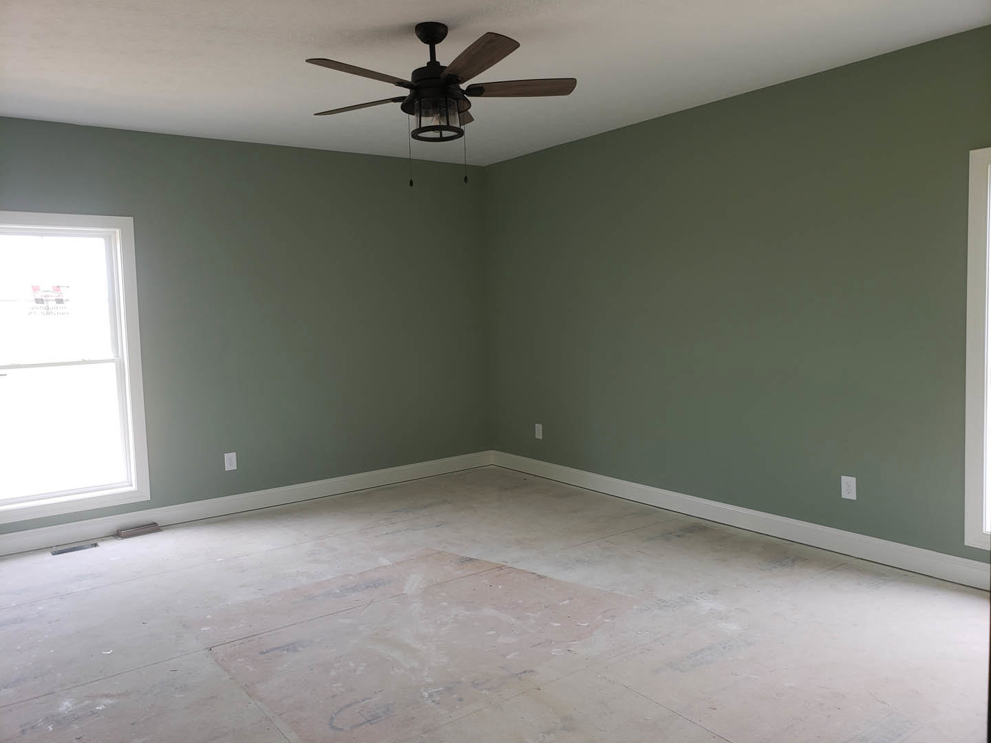 Ceiling fan with integrated light fixture, white walls and flooring, green accent wall, window with white trim, white door frame, minimalist interior finishes