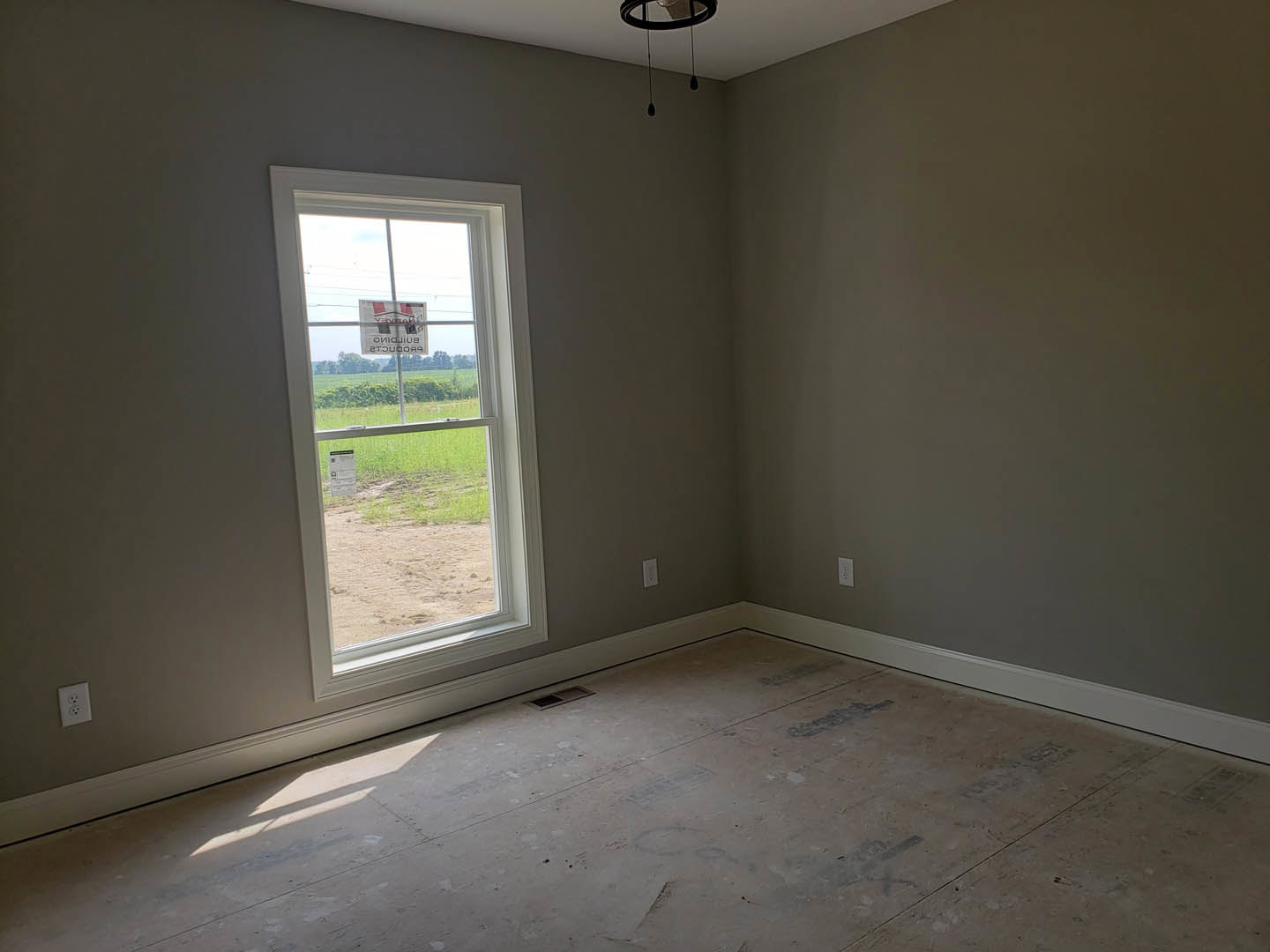 Sunlit room with plaster walls, wood flooring, large window overlooking grassy field, modern light fixture hanging from ceiling