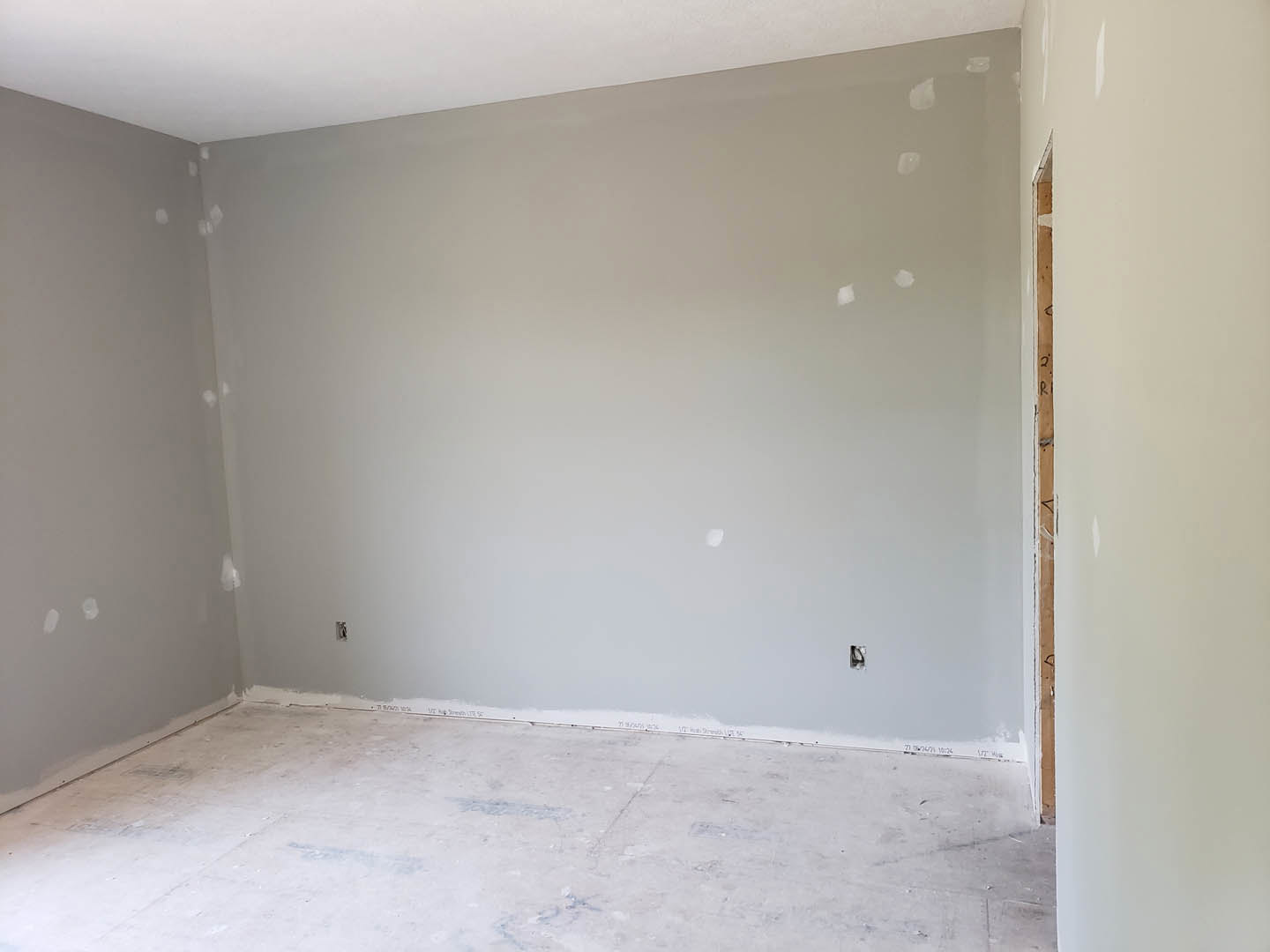 Concrete floor and white plaster walls in an unfinished room with a wood-framed doorway and exposed ceiling.