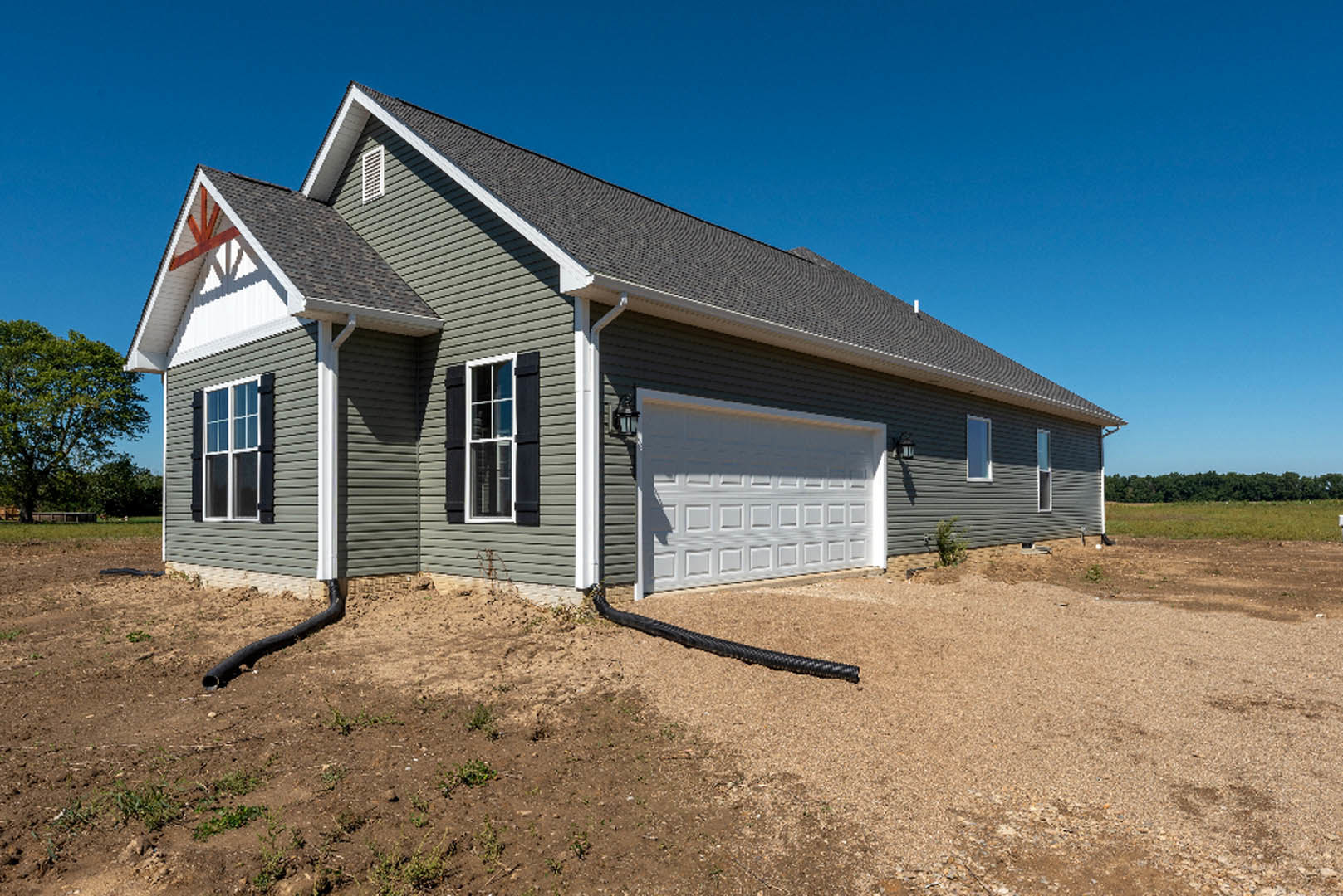 Modern house exterior with attached garage, white siding, large windows, green-leafed tree in front yard, black drainage pipe along foundation