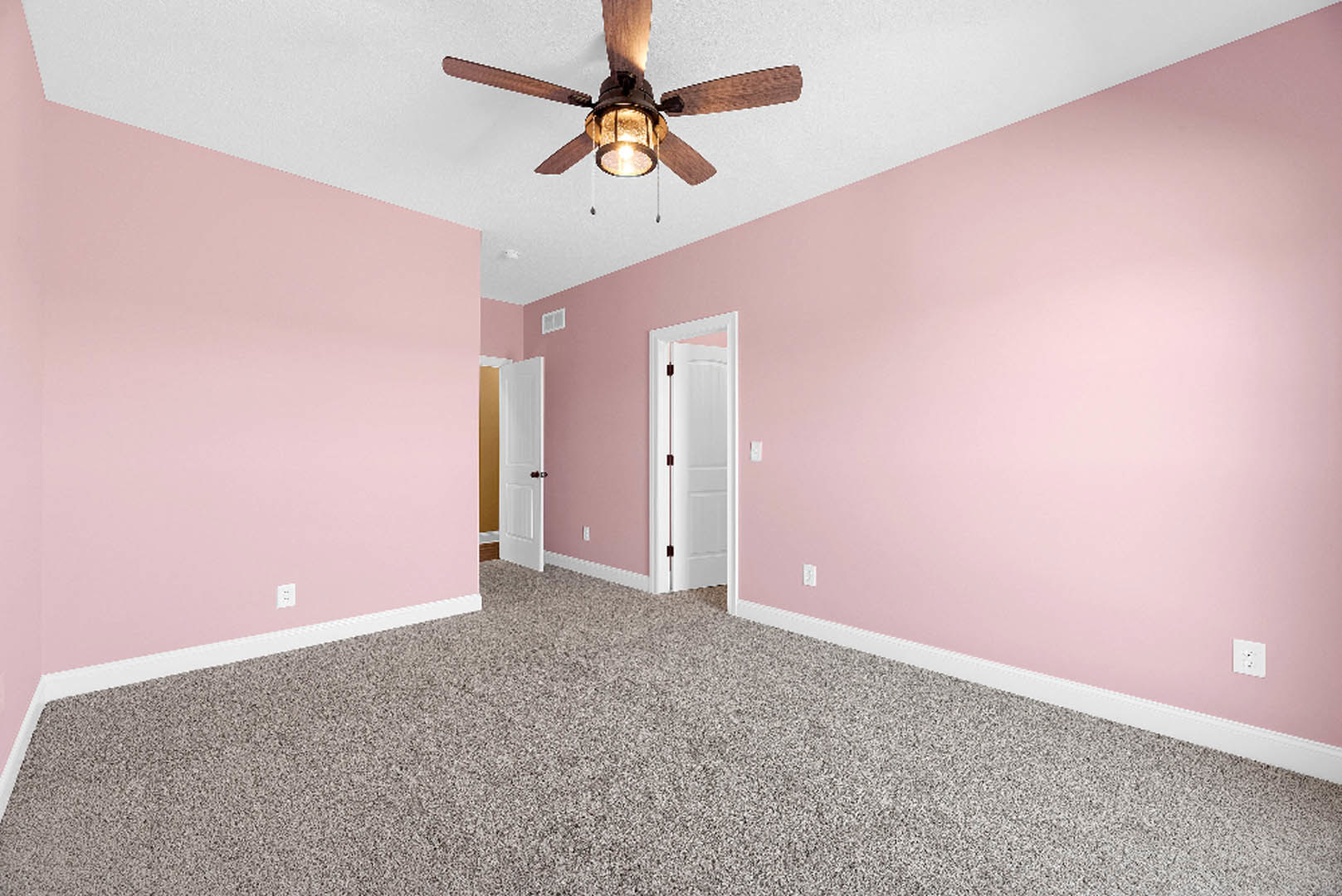 Carpeted room with pink plaster walls, white door featuring a black handle and red string, ceiling fan with light, white electrical outlet