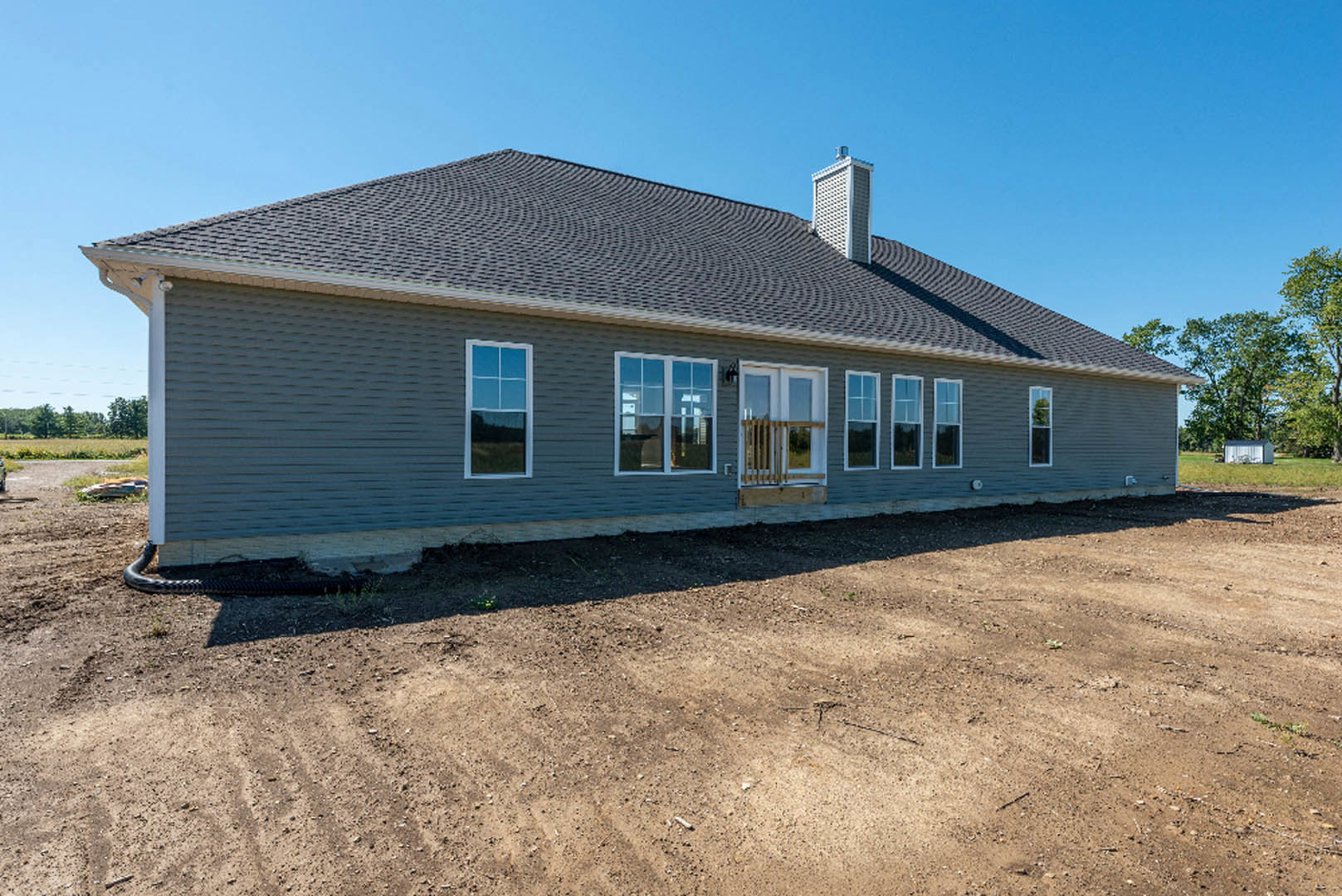 White house with multiple windows and chimney, surrounded by a dirt field under a clear blue sky
