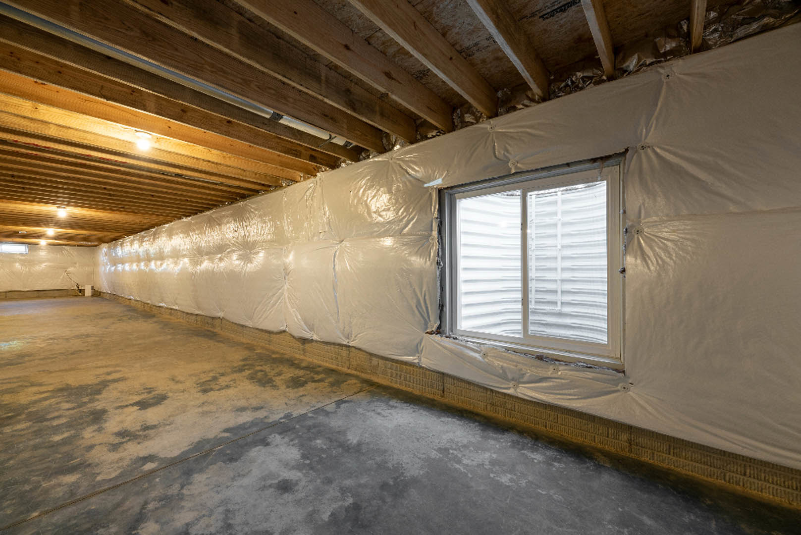 Room with a concrete floor, white-framed window with sheer curtain, and wall covered in translucent plastic sheeting
