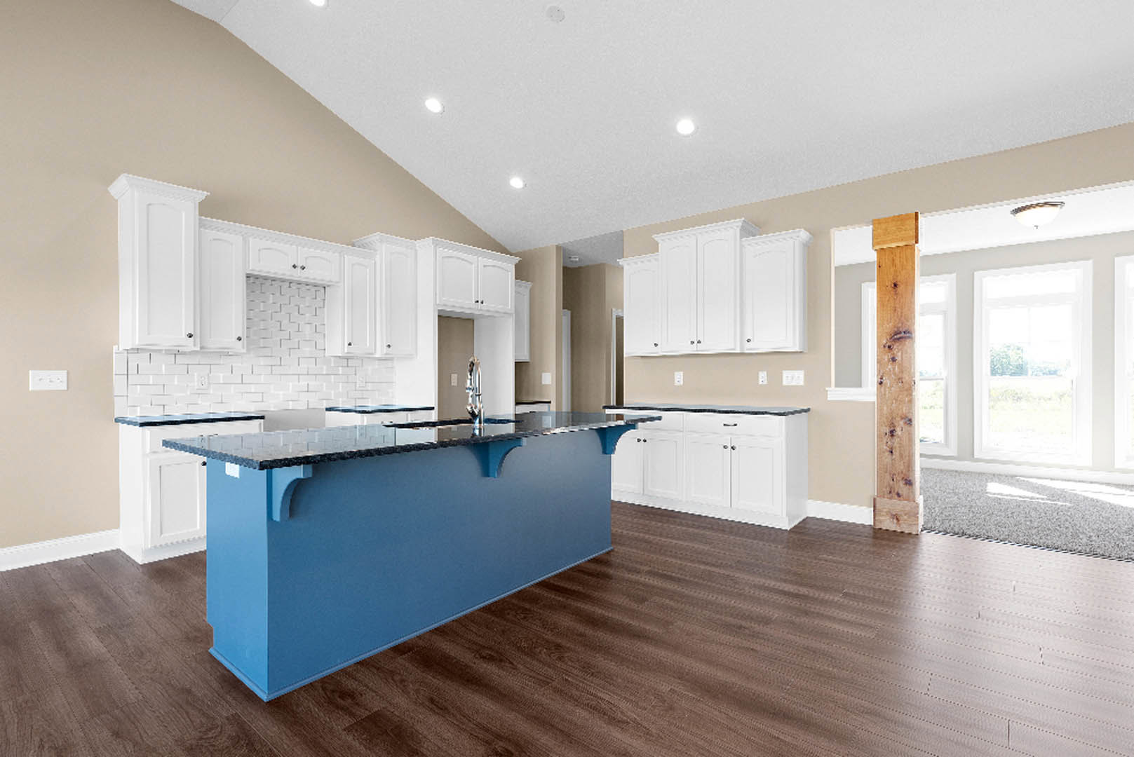 Blue kitchen island with white quartz countertop, white shaker cabinets, stainless steel sink, light wood flooring, and large window with white trim.