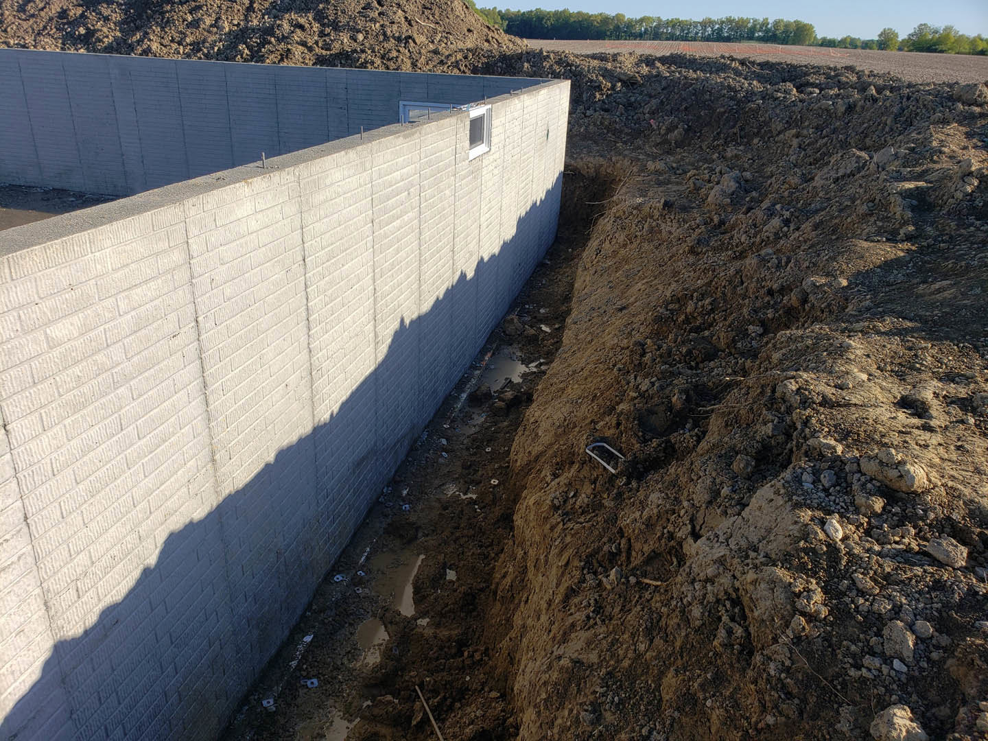 Concrete exterior wall with circular hole in the ground, surrounded by soil and outdoor space under open sky