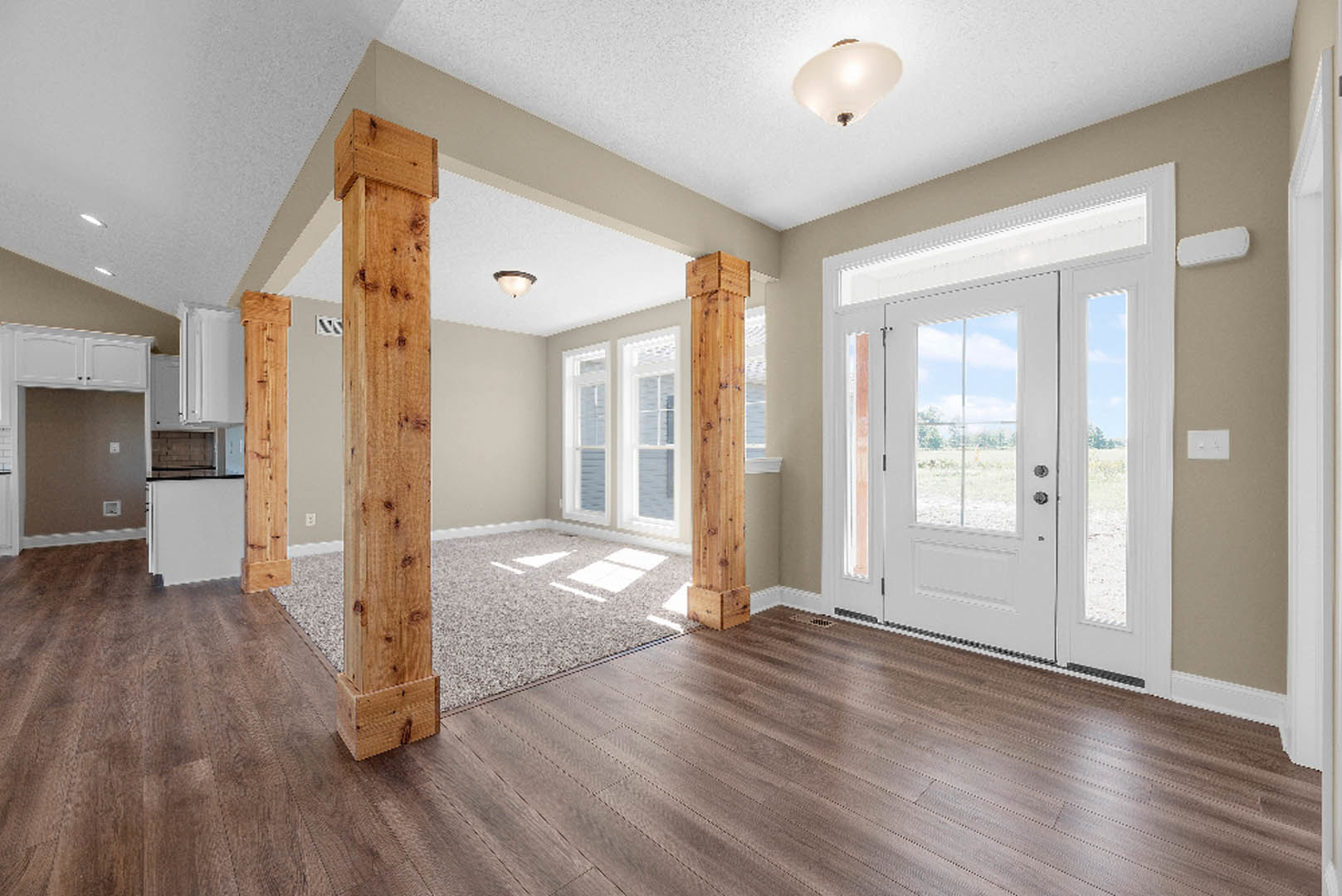 Open room with wood flooring, wood pillars, white plaster walls, and a white door featuring glass windows and brown trim