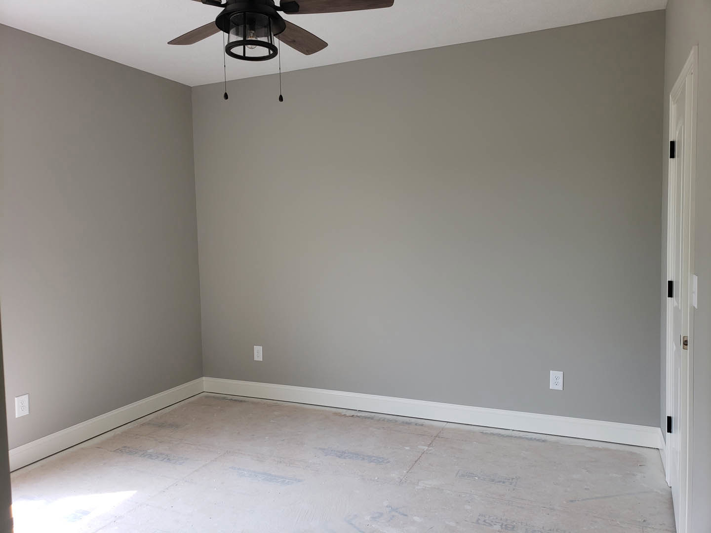 Ceiling fan with integrated light fixture mounted on smooth white ceiling, white door with black hardware, white flooring, and soft lighting illuminating the room.