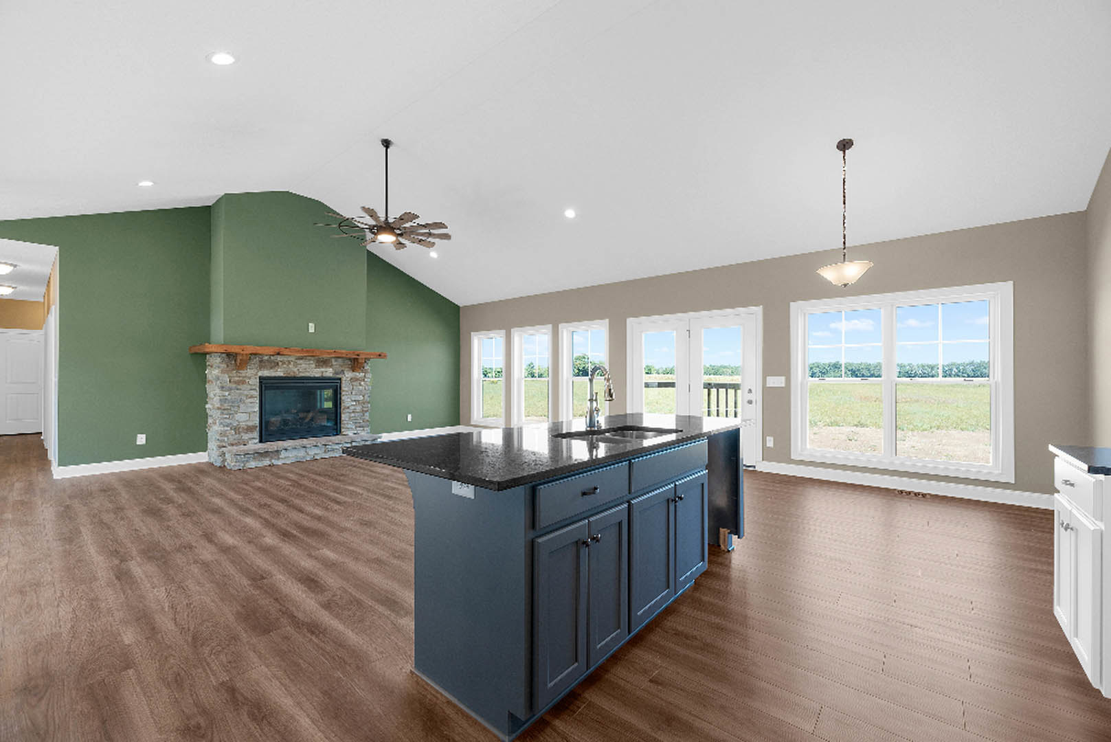 Open-concept kitchen and living room featuring a central island with sink, modern cabinetry, wood flooring, glass-door fireplace, tall floor lamp, and large window overlooking a