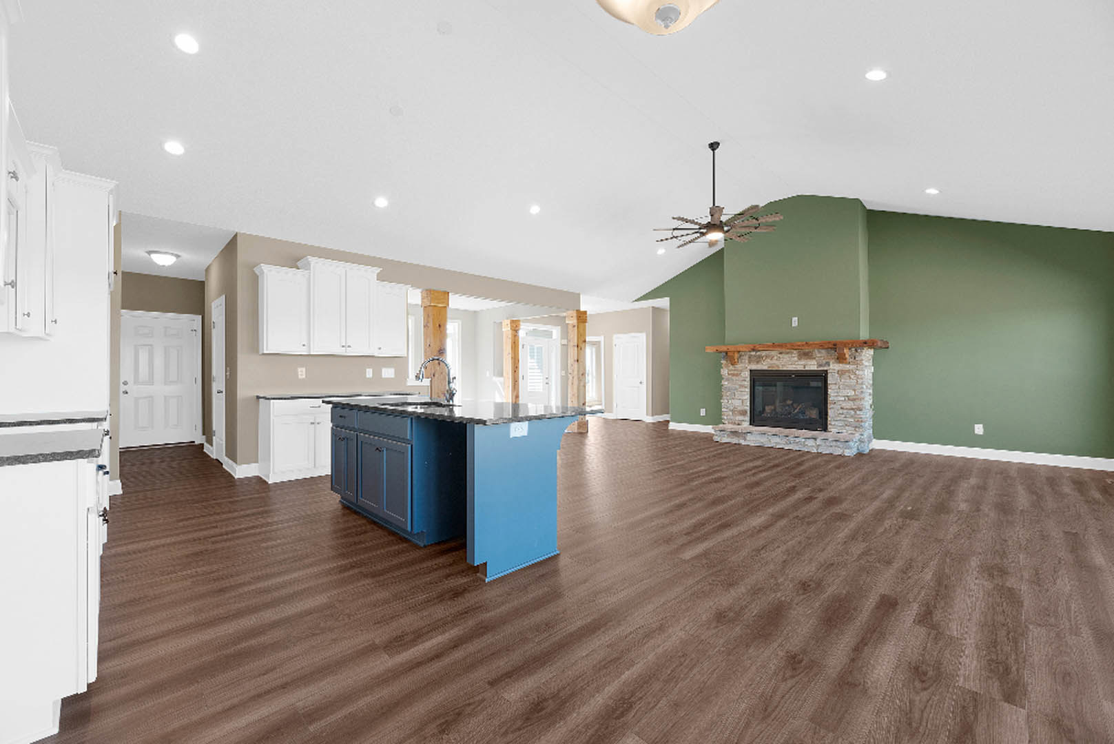 Open-concept kitchen and living room featuring a blue kitchen island, matching blue countertop, glass-door fireplace, white cabinetry, ceiling fan with light, and white door with