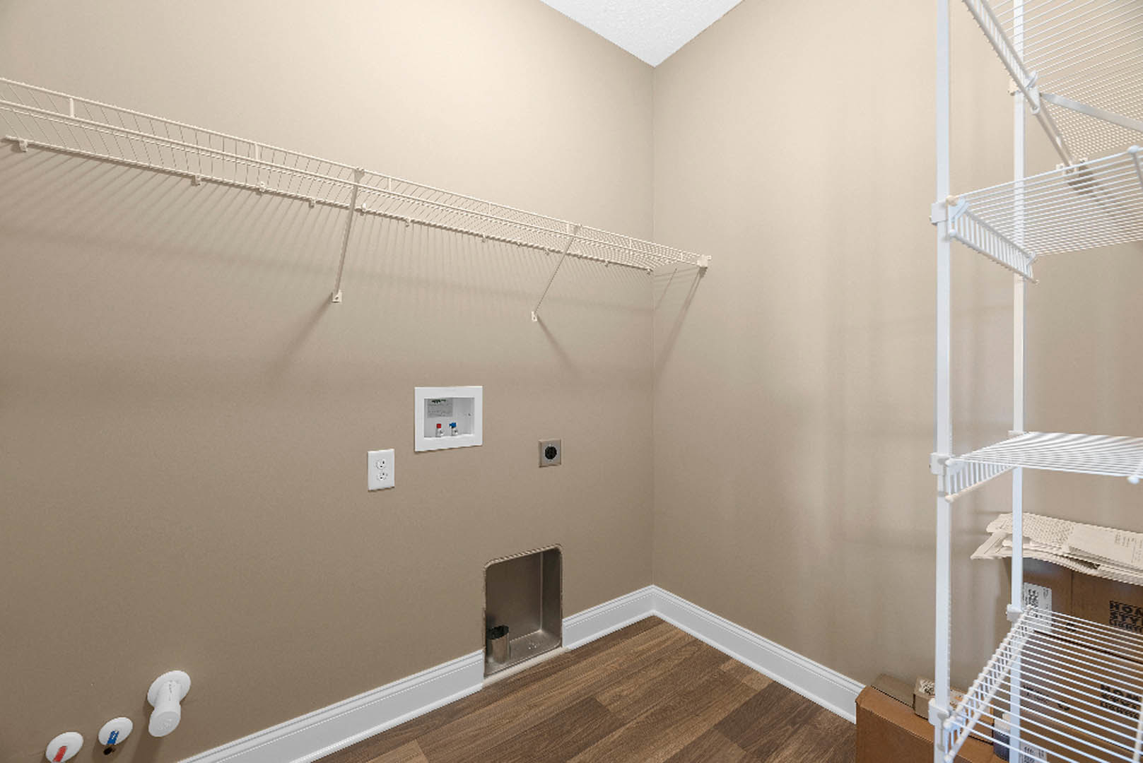 Wood floor room with white wall-mounted rack, white electrical outlet, framed utility box with red and blue valves, and blue object in foreground