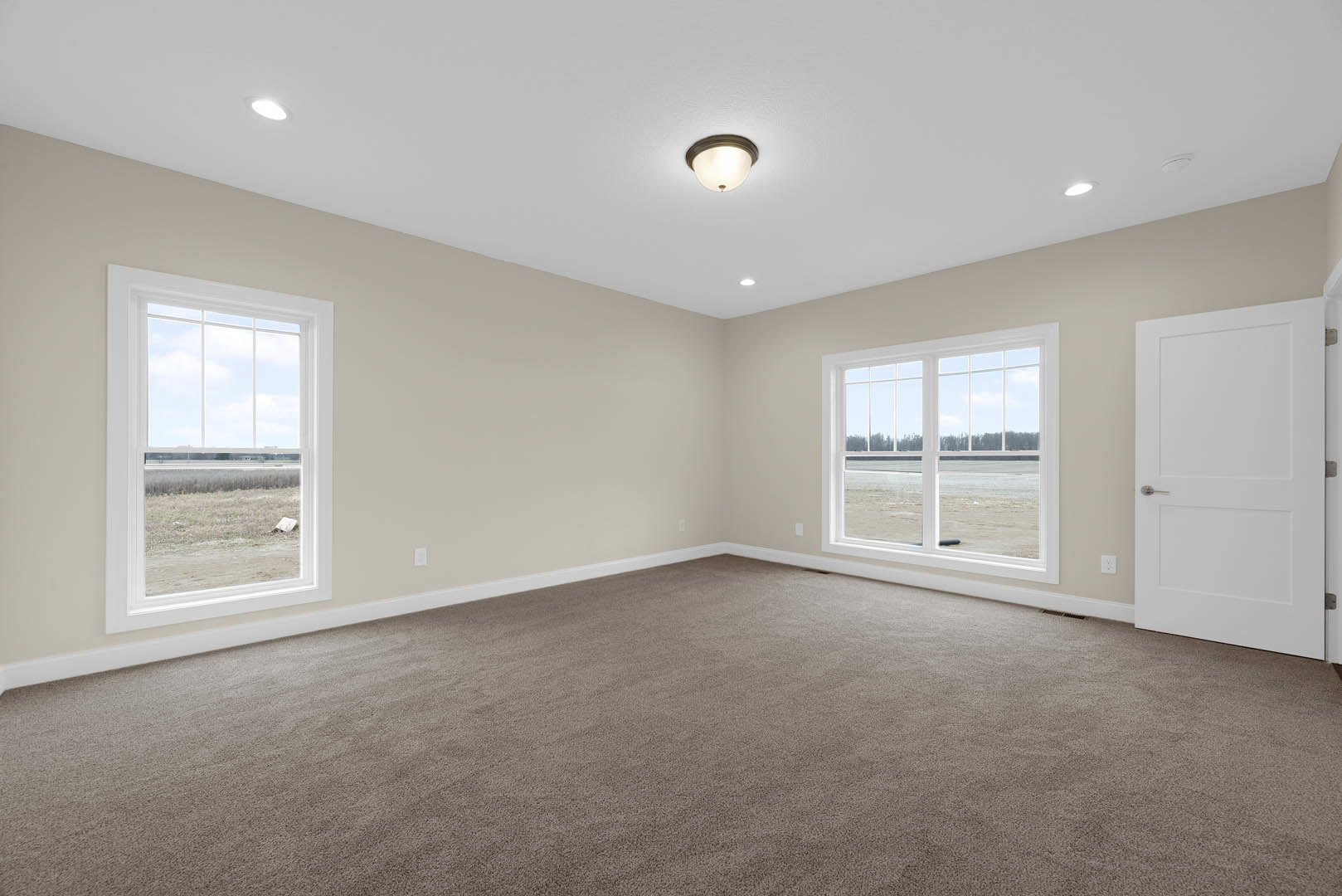 Carpeted room with large windows, white walls, ceiling light fixture, and white door with silver handle