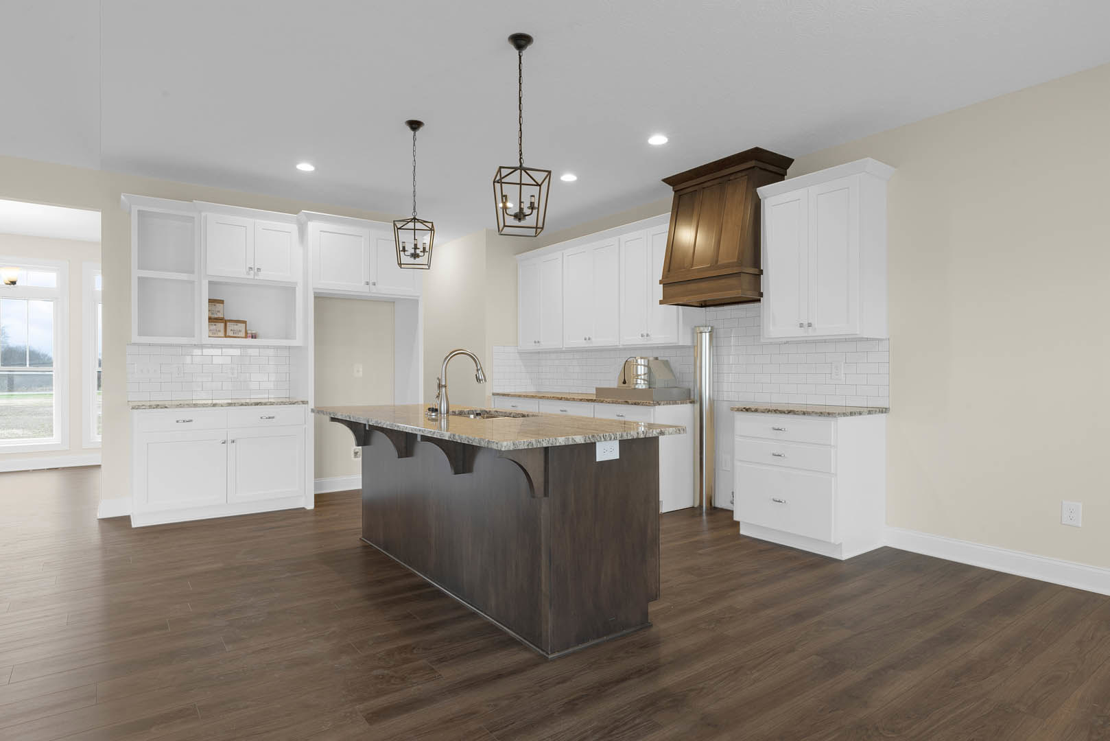 Kitchen with white shaker cabinets, marble-topped island, wooden range hood, pendant lights suspended by chains, hardwood flooring, stainless steel sink, and metal container on