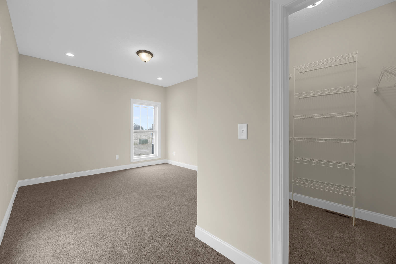 Bright room with light-colored plaster walls, wood flooring, white wall outlet, built-in white shelf, ceiling light fixture, door, and window with outdoor view