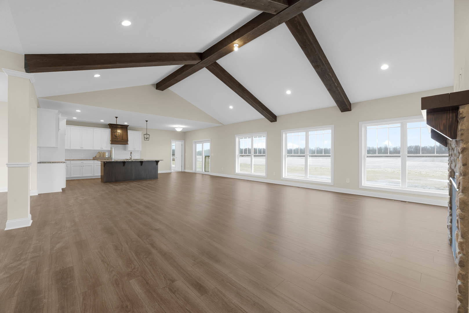 Spacious room featuring hardwood floors, exposed wooden ceiling beams, plaster walls, large window with outdoor view, modern ceiling light fixture, and built-in wall shelf