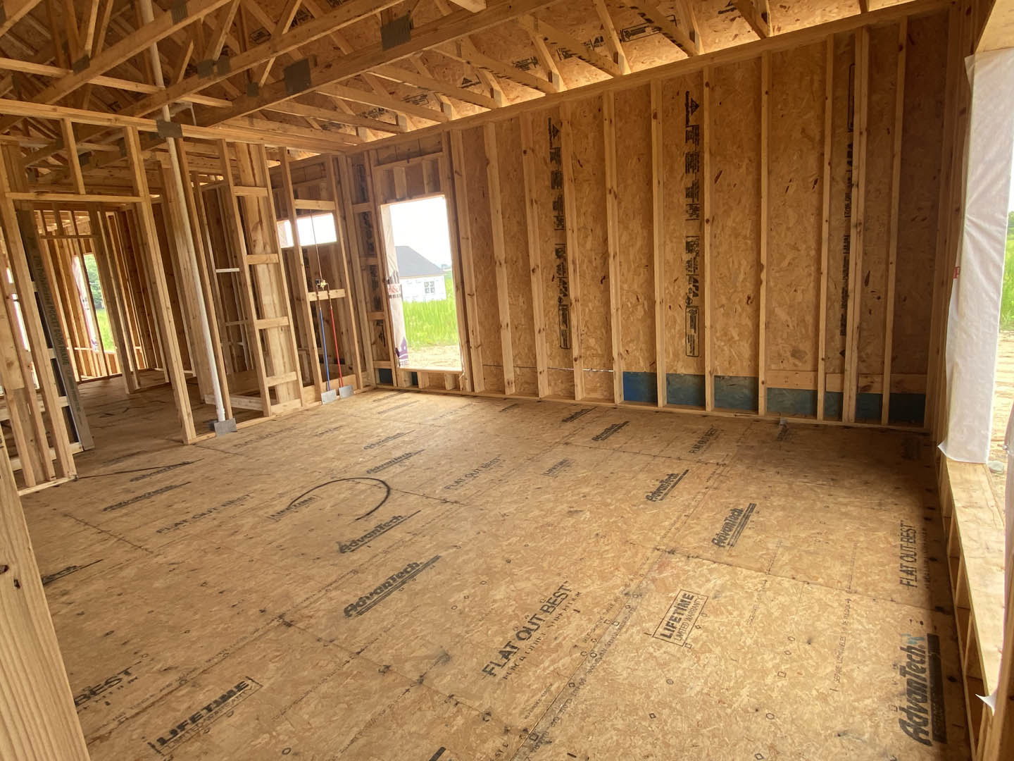 Open room with exposed wood ceiling beams, plywood flooring, wooden door, and window partially covered by a white sheet