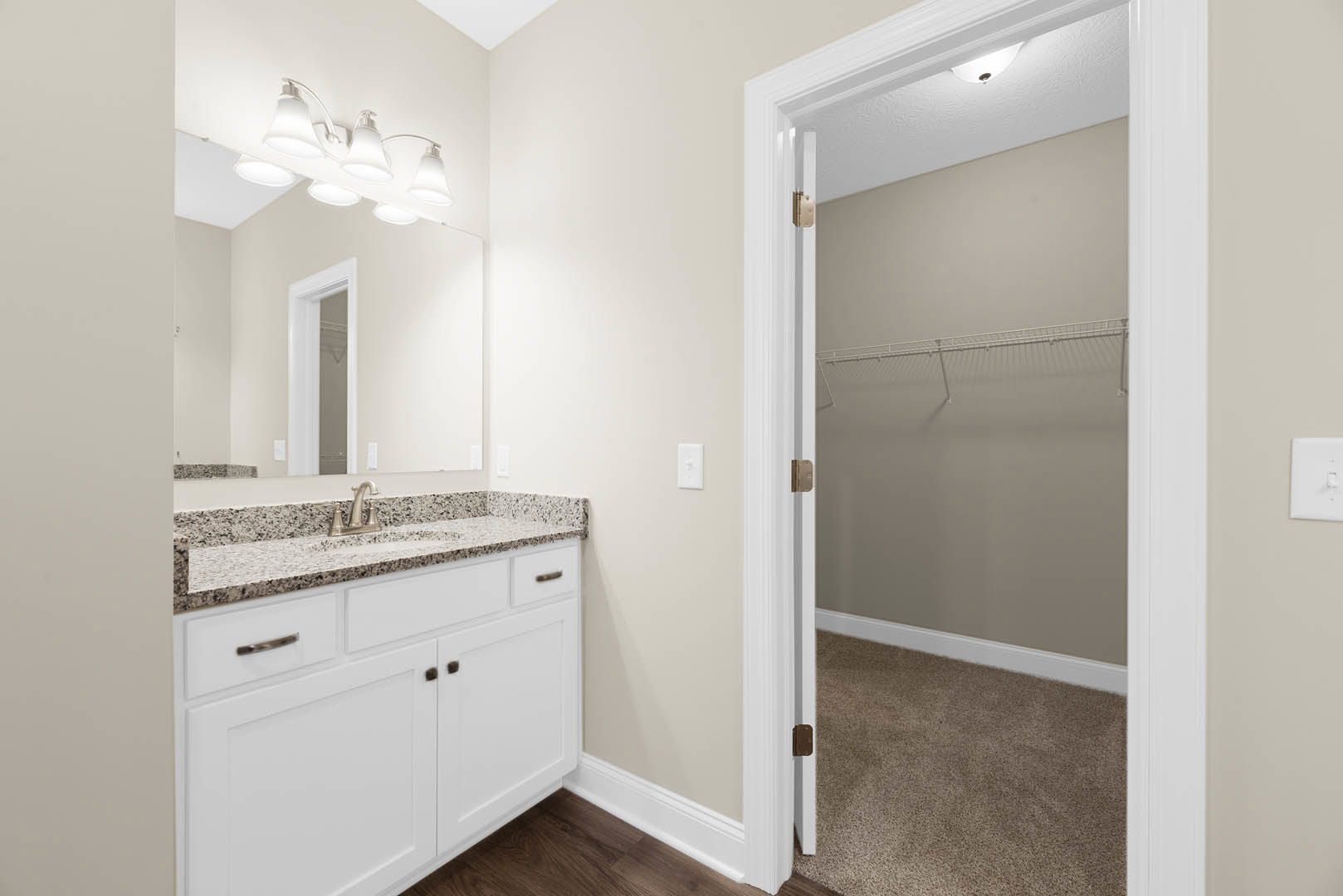 Bathroom with marble-topped white vanity, rectangular mirror, chrome faucet, white tile floor, recessed ceiling lights, white door, and adjacent closet with matching door.