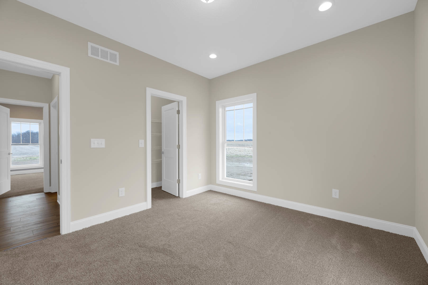 Open white door with silver knobs leading to a room featuring hardwood floors, white staircase, carpeted area, and large window overlooking the ocean.