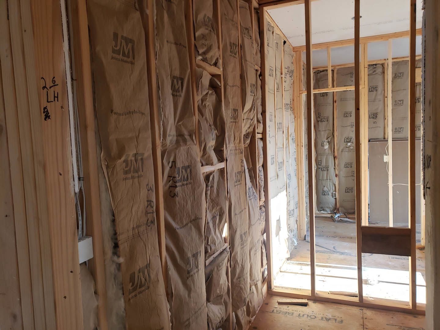 Room with exposed wood framing, unfinished plaster walls, and a wooden door; natural light from a window highlights construction materials.